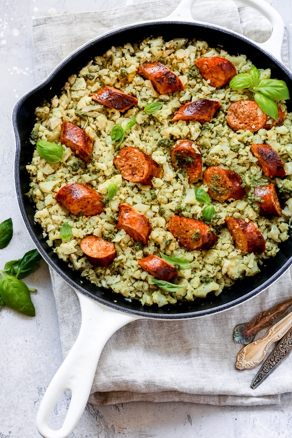 Italian Sausage Cauliflower Rice Skillet with pesto and basil leaves on top