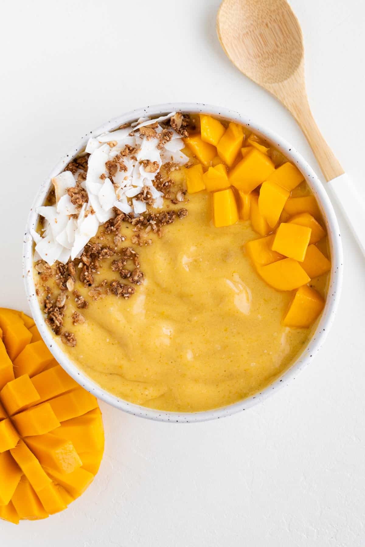 a mango turmeric smoothie bowl alongside a bamboo spoon and sliced mango