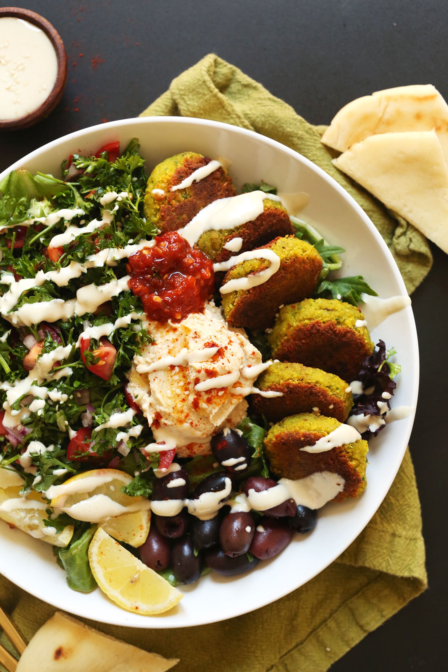 Serving of our vegan Mediterranean Bowl with hummus, falafel, tahini sauce, olives, and pita