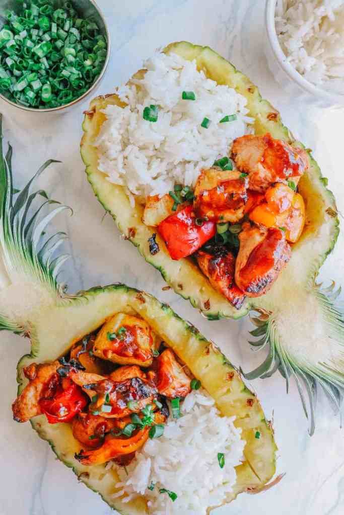 chicken stir fry with pineapple in a hollow pineapple topped with green onions.