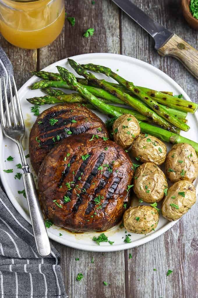 Overhead view of portobello mushroom steaks with potatoes and asparagus on the side. 